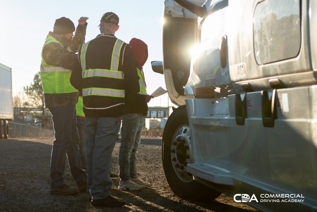 Three instructors standing next to semi truck, sun reflecting off cab