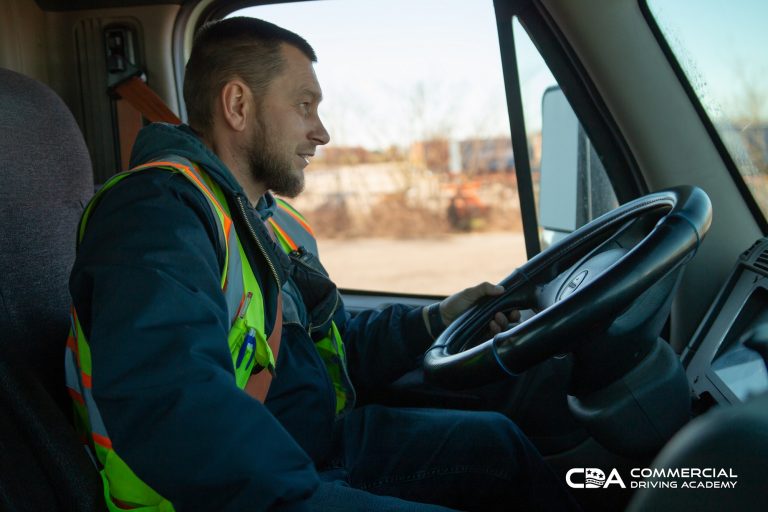 Truck driver holding steering wheel in cab and looking straight ahead. Side view.