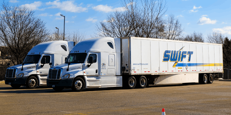 Two Swift semi trucks parked in concrete lot
