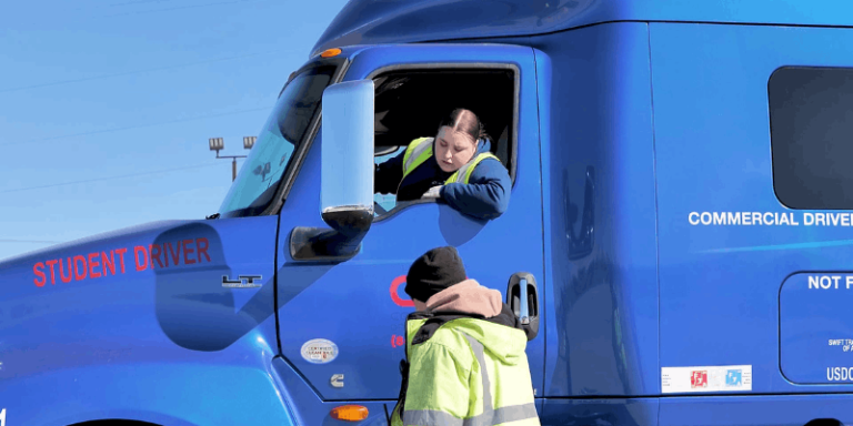 Female trucker leaning out of cab window, talking to instructor standing