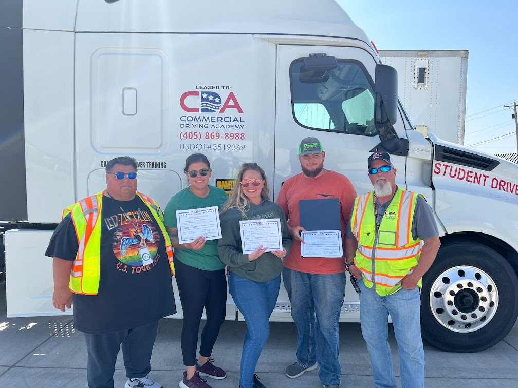 Three CDA graduates and two instructors standing in front of CDA semi truck