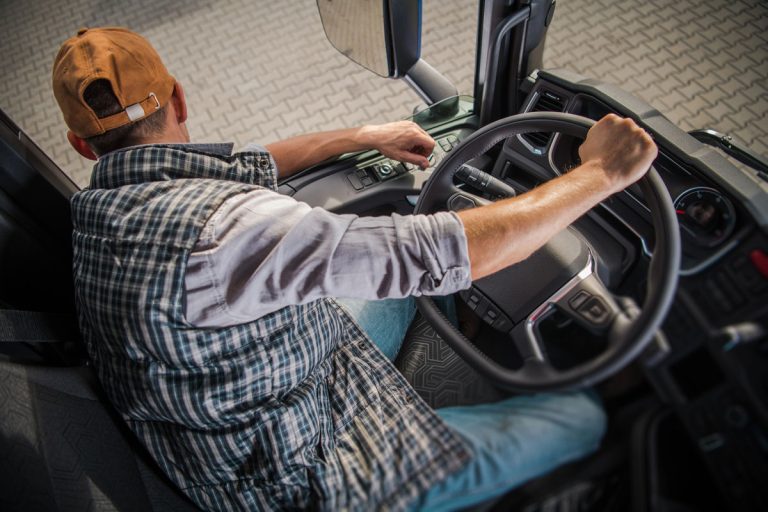 Birdseye view of trucker looking out cab window with his hand on the steering wheel