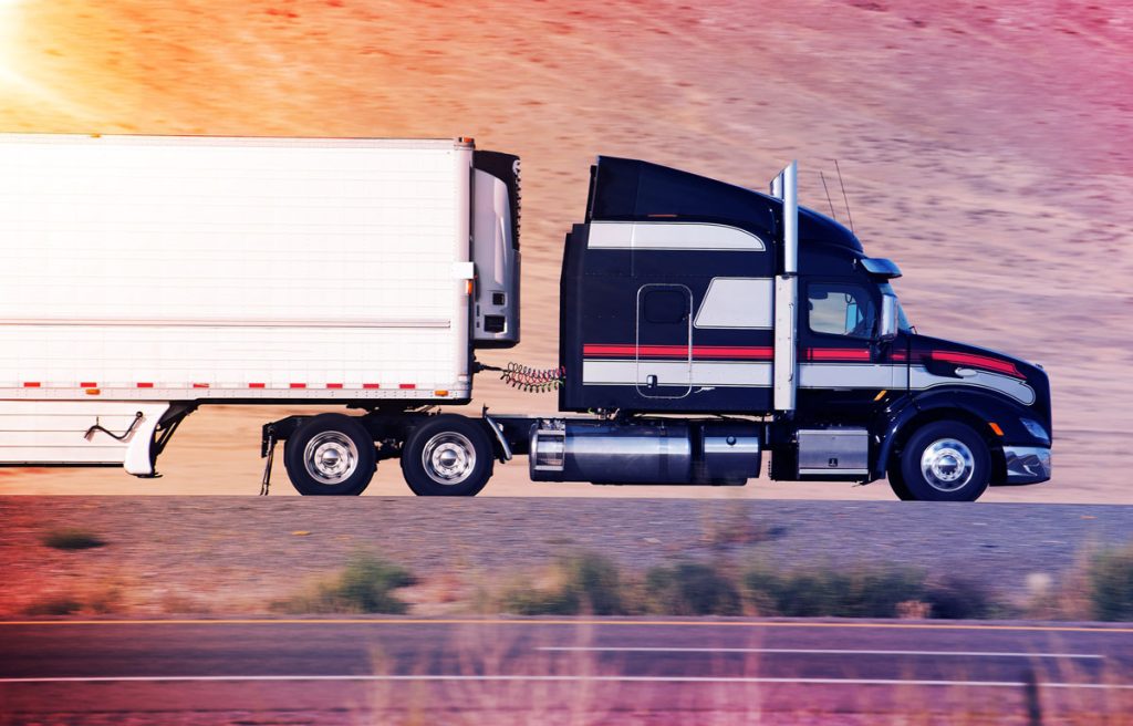 Black semi truck on the road during sunset, pink and orange skies