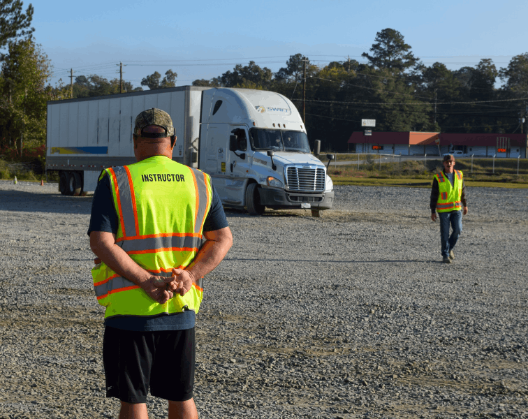 Two instructors standing in training yard, guiding semi truck