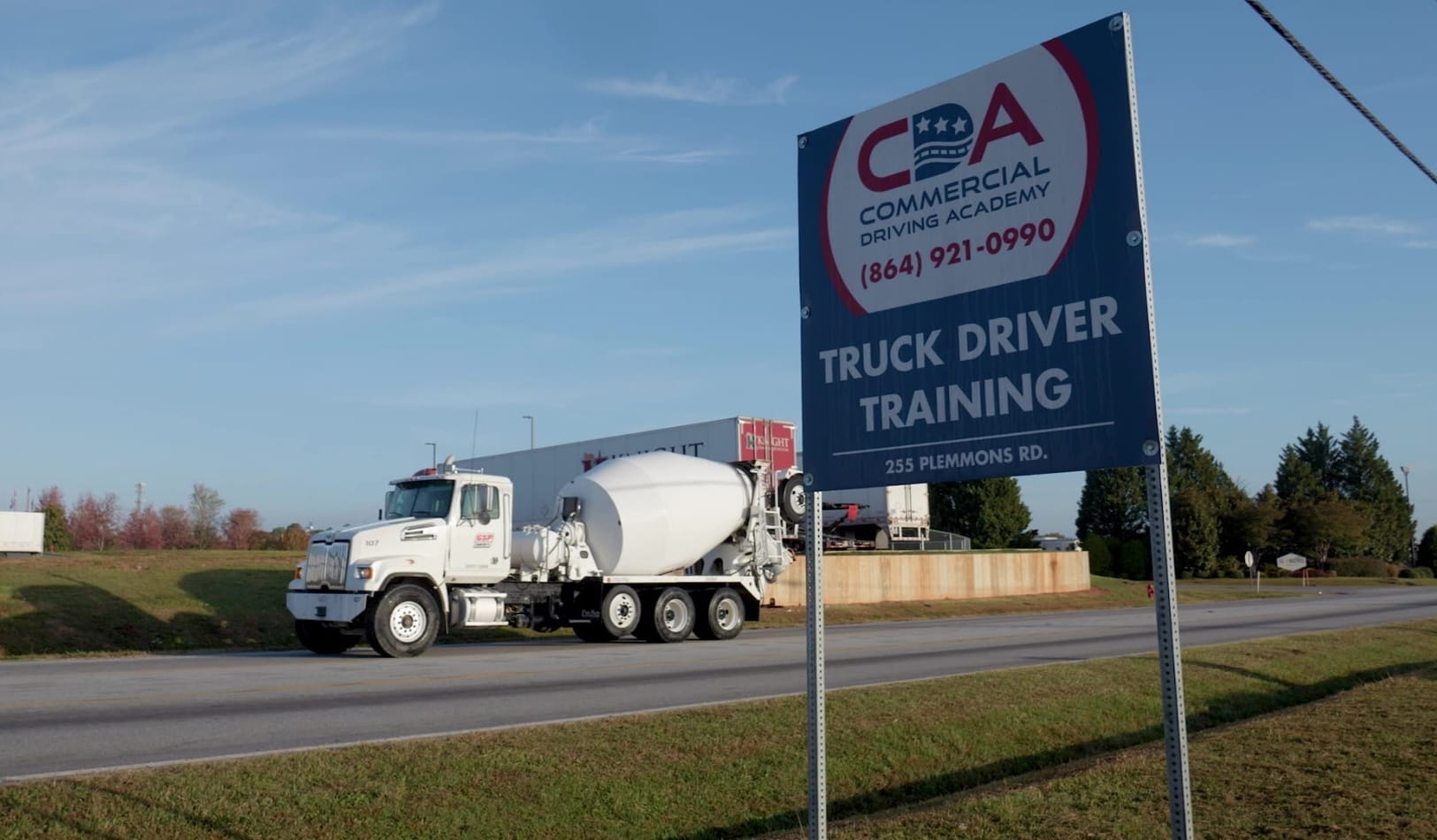 Closeup of CDA Truck Driver Training entry sign. Cement truck on road in back.