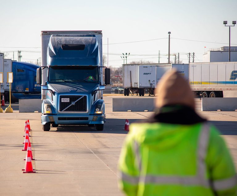 Instructor standing in front of camera, out of focus. Semi truck facing toward instructor.