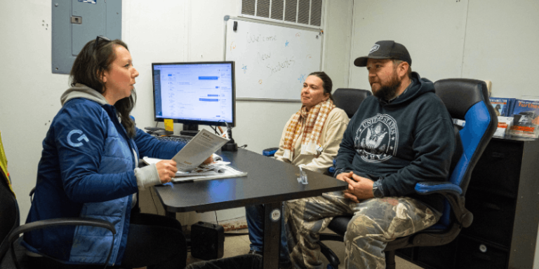 Admissions advisor holding papers and speaking with two potential students at desk