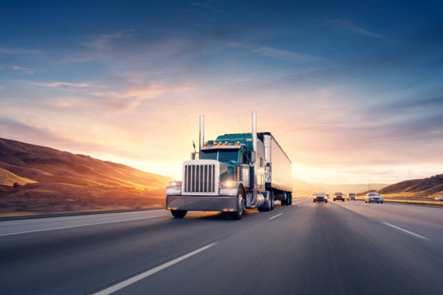 An American commercial truck drives down the highway at sunset.