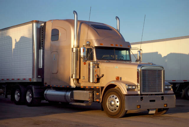 An American commercial semi-truck is parked in a lot beside other commercial trucks.